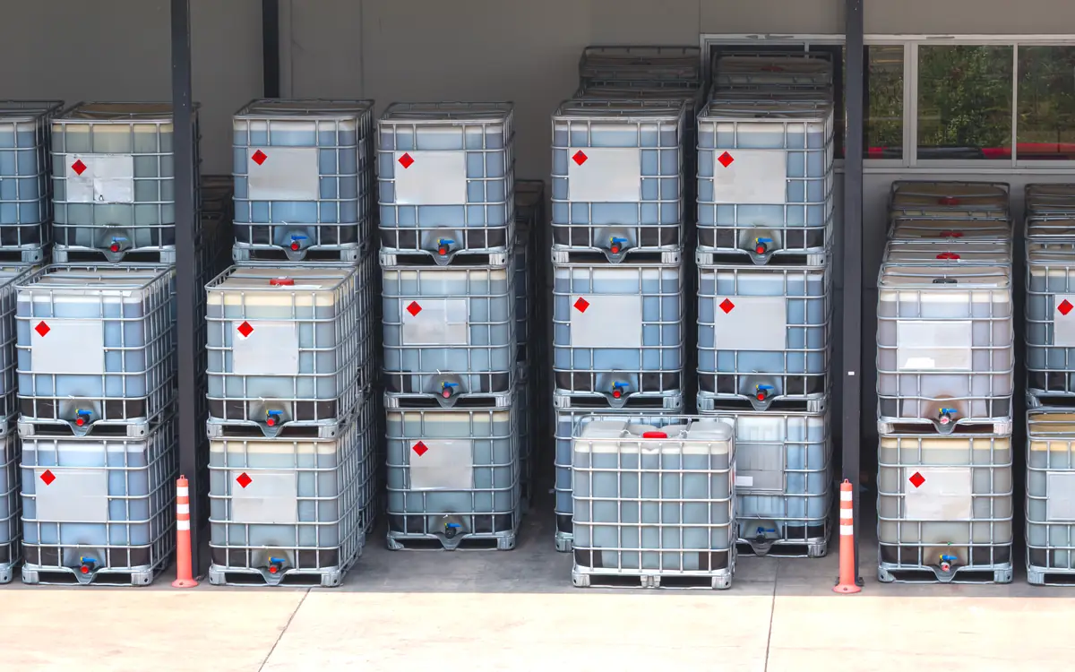 Metal IBC containers for liquids lined up in rows, with red labels