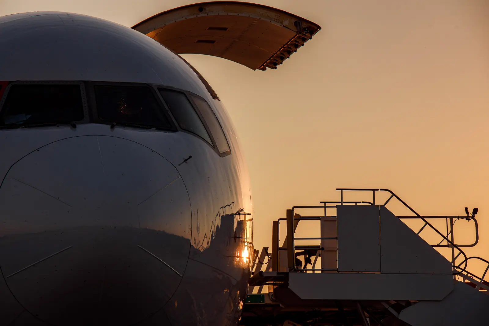 The nose of a cargo aircraft with its door raised and a loading platform, at sunset