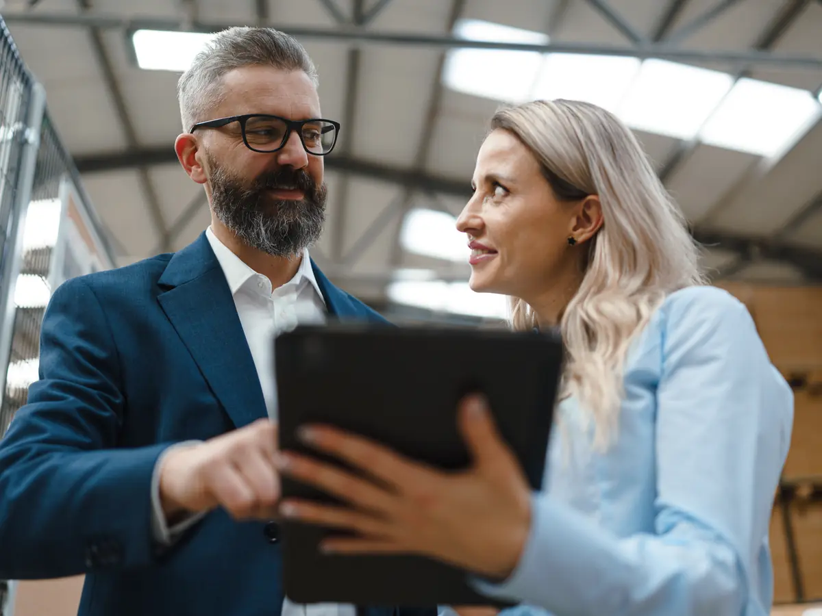 A consultant and a client talking over a tablet in a bright warehouse