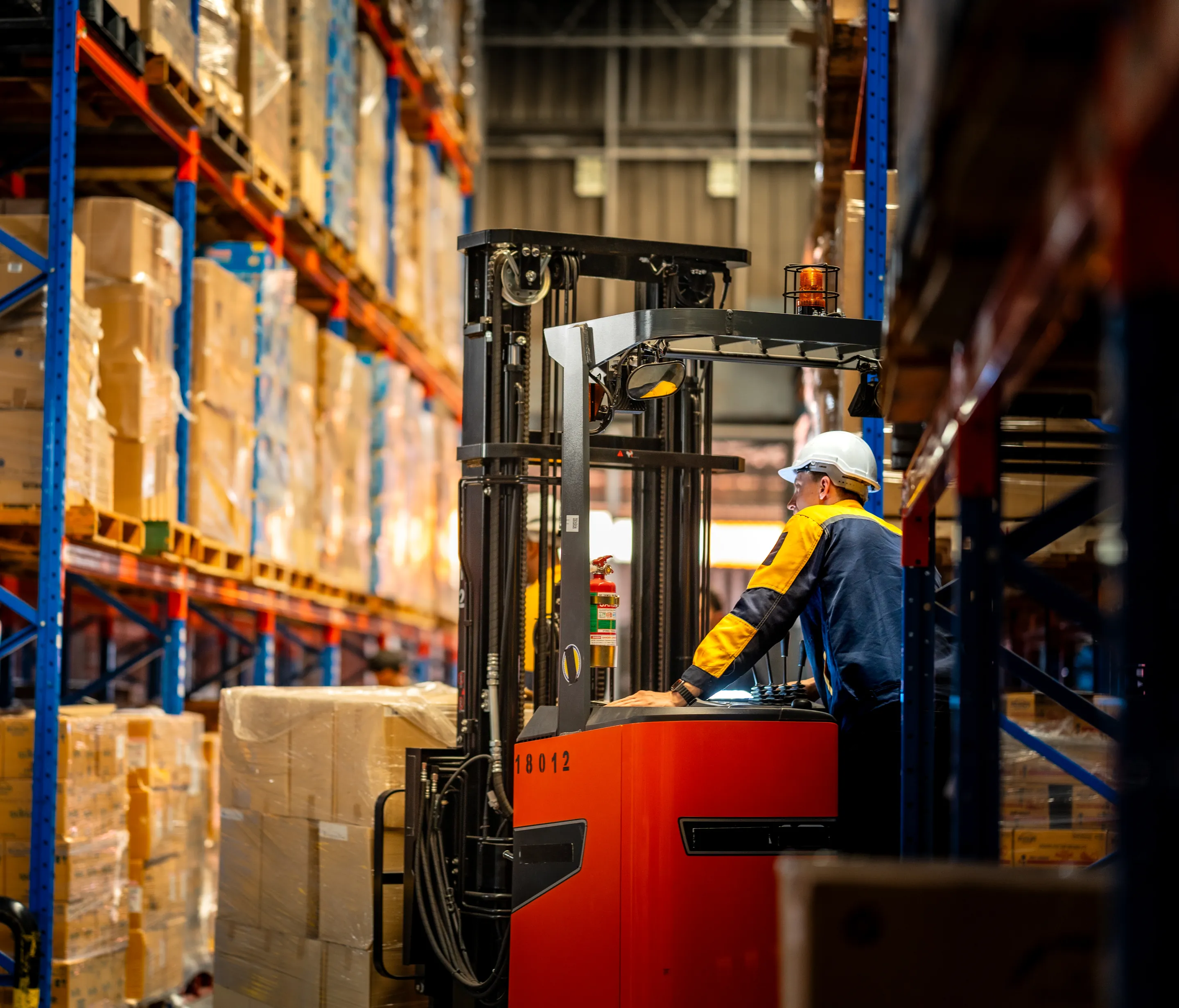 A forklift operator in a logistics warehouse with tall racks and pallets