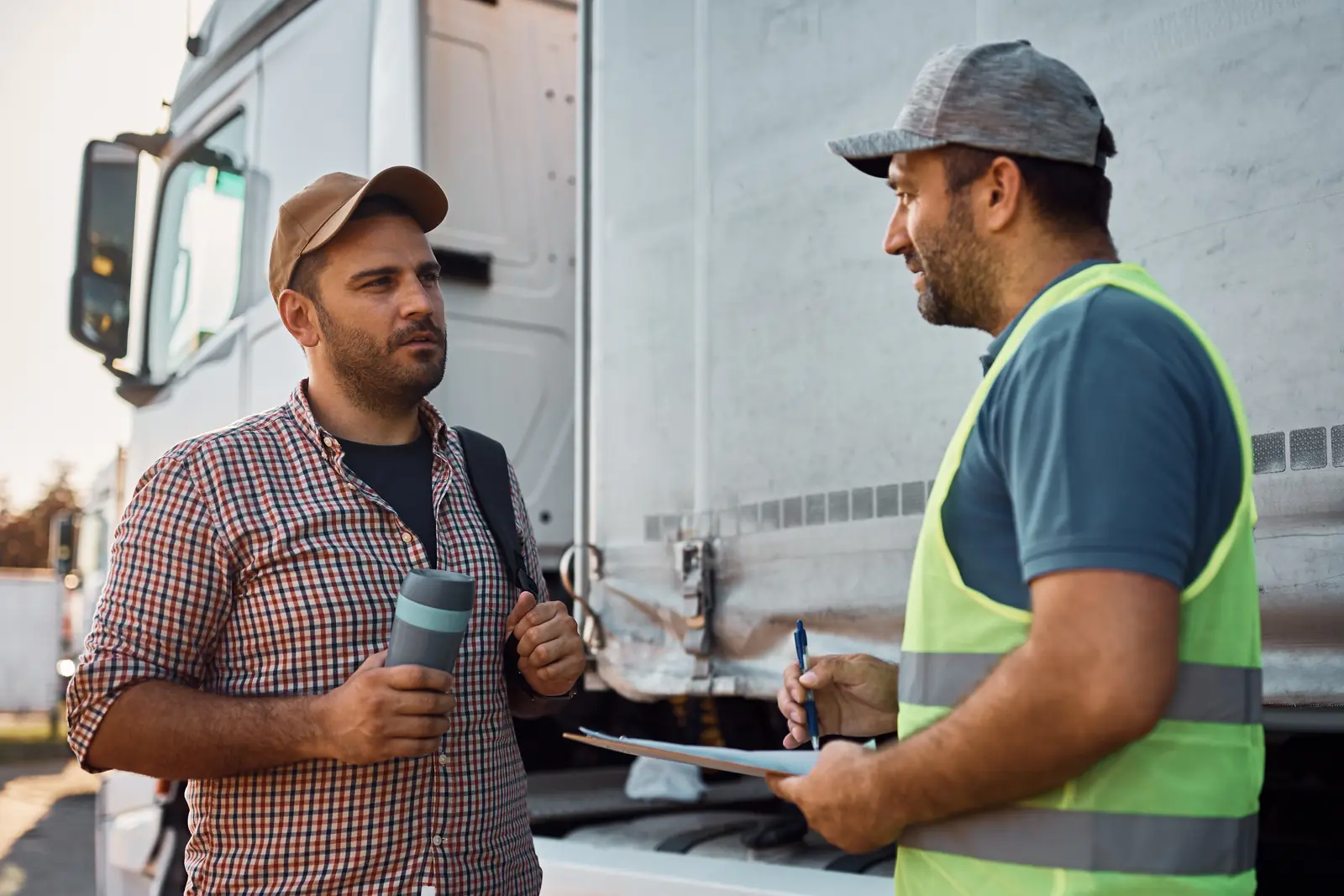 A man in a high-visibility vest checking the transport documents with a driver, next to a semi-trailer