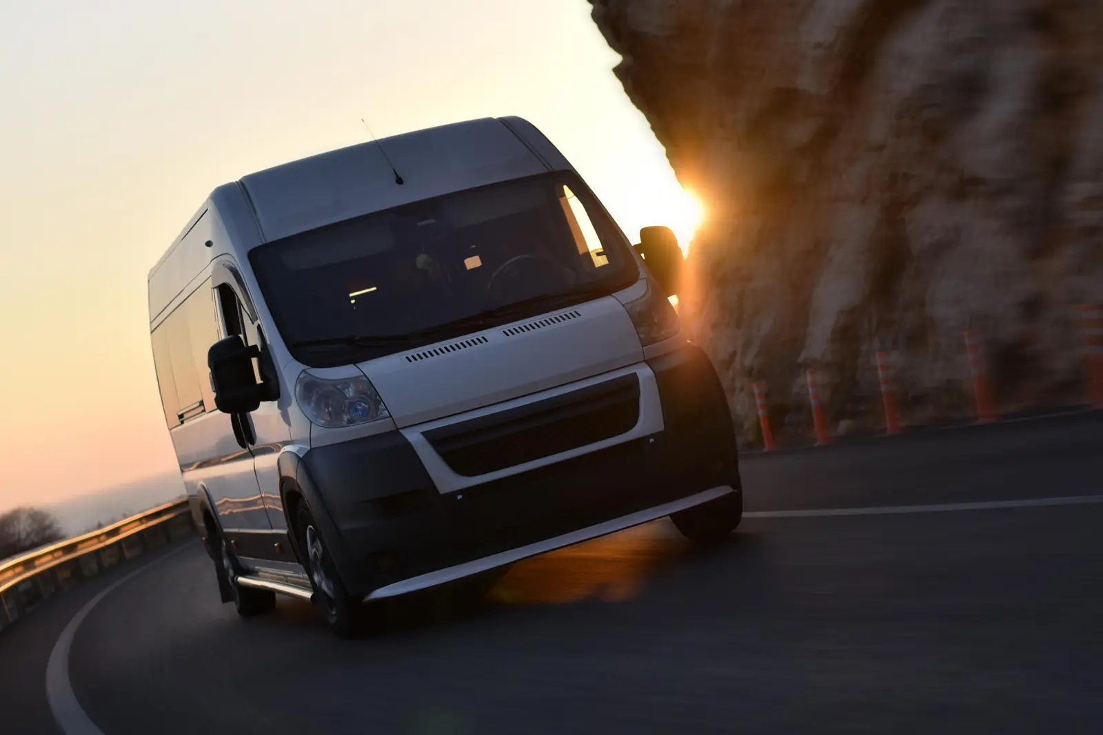 White delivery van taking a bend on a mountain road at sunset
