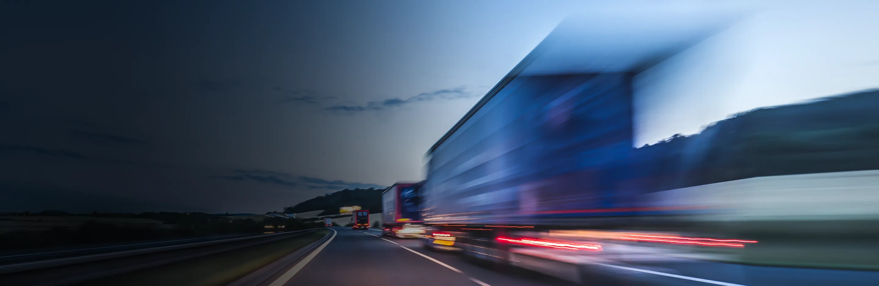 Trucks in motion on a motorway at dusk, blue sky, an image with a motion-blur effect