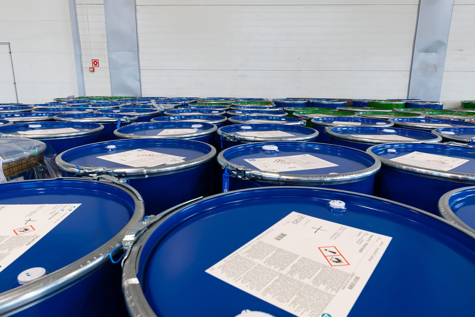 Rows of blue drums with hazard labels, stored in a warehouse